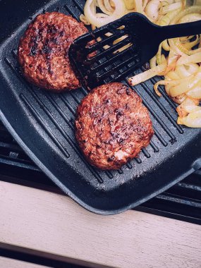 Cooking minced beef burger on cast iron grill skillet outdoors, red meat on frying pan, grilling food in the garden, English countryside living concept