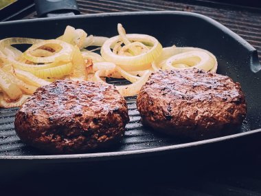 Cooking minced beef burger on cast iron grill skillet outdoors, red meat on frying pan, grilling food in the garden, English countryside living concept