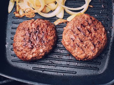 Cooking minced beef burger on cast iron grill skillet outdoors, red meat on frying pan, grilling food in the garden, English countryside living concept