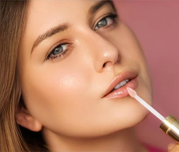 Beauty, makeup and skincare cosmetics model face portrait on pink background, beautiful woman applying lip gloss, perfect healthy skin glow, facial care closeup