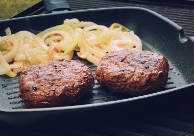 Cooking minced beef burger on cast iron grill skillet outdoors, red meat on frying pan, grilling food in the garden, English countryside living concept