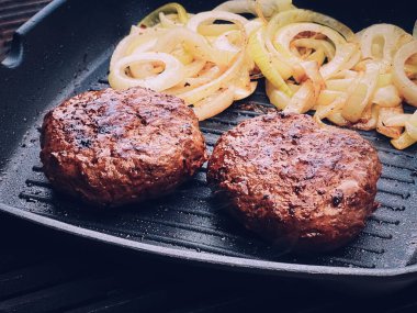 Cooking minced beef burger on cast iron grill skillet outdoors, red meat on frying pan, grilling food in the garden, English countryside living concept