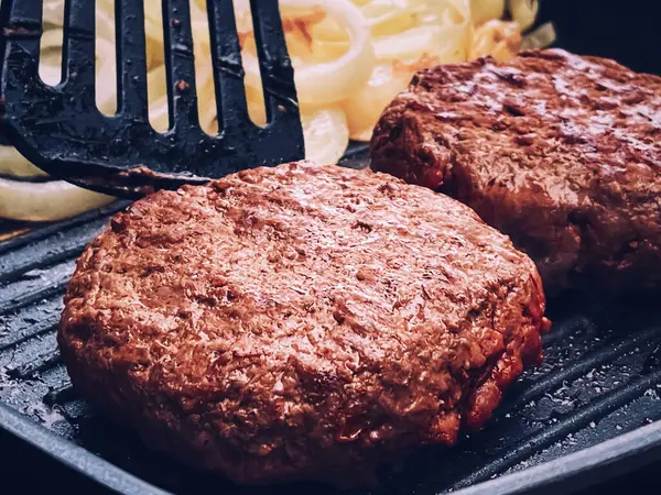 Cooking minced beef burger on cast iron grill skillet outdoors, red meat on frying pan, grilling food in the garden, English countryside living concept