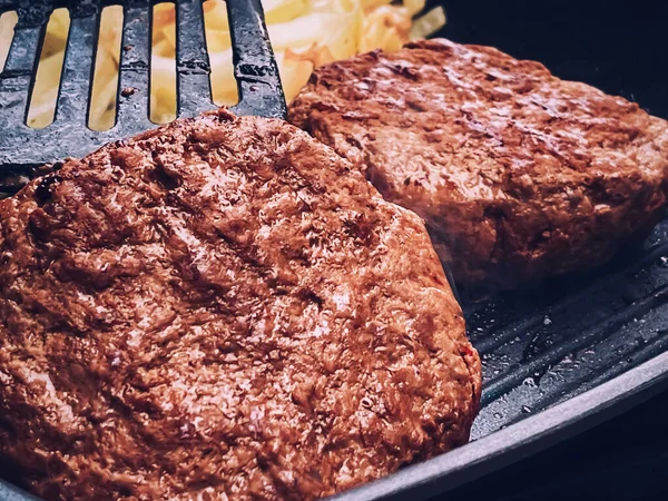Cooking minced beef burger on cast iron grill skillet outdoors, red meat on frying pan, grilling food in the garden, English countryside living concept