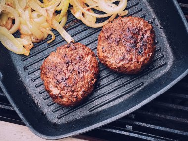 Cooking minced beef burger on cast iron grill skillet outdoors, red meat on frying pan, grilling food in the garden, English countryside living concept