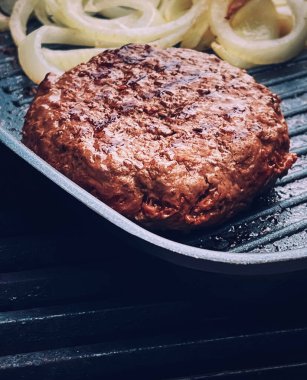 Cooking minced beef burger on cast iron grill skillet outdoors, red meat on frying pan, grilling food in the garden, English countryside living concept