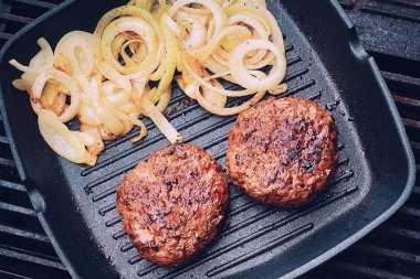 Cooking minced beef burger on cast iron grill skillet outdoors, red meat on frying pan, grilling food in the garden, English countryside living concept