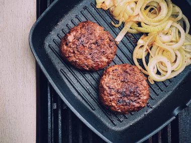 Cooking minced beef burger on cast iron grill skillet outdoors, red meat on frying pan, grilling food in the garden, English countryside living concept