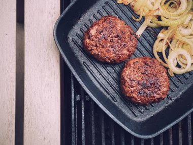 Cooking minced beef burger on cast iron grill skillet outdoors, red meat on frying pan, grilling food in the garden, English countryside living concept