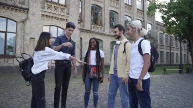 Çok ırklı öğrencilerden oluşan neşeli bir grup el ele tutuşuyor.