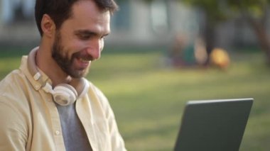 Bilgisayarlı gülümseyen erkek öğrenci dışarıda ders çalışıyor.