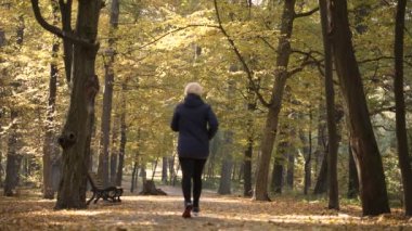 Sporty aged woman running along park alley