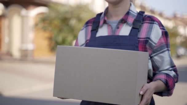 Улыбающаяся курьер идет с картонной коробкой — стоковое видео