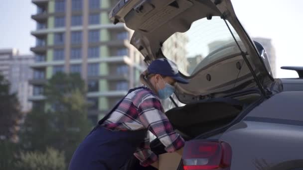 Femme de livraison masquée prenant des boîtes du coffre de la voiture — Video