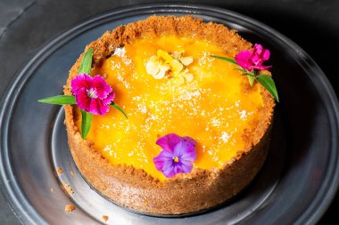 Homemade mango and coconut cheesecake with fresh edible flowers.