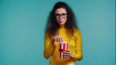 Kıvırcık, genç bir kadın elinde patlamış mısır kovası tutuyor ve mavi üzerine izlenmiş bir film izliyor.