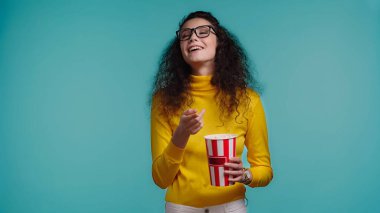 Mutlu genç bir kadın elinde patlamış mısır kovası tutuyor ve mavi üzerine izlenmiş bir film izliyor.  