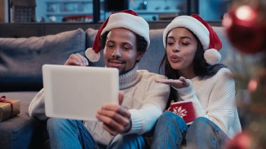 Mutlu Afro-Amerikan erkeği, kadının yanında hava öpücüğü yolluyor ve video çağrısı sırasında dijital tablete bakıyor.