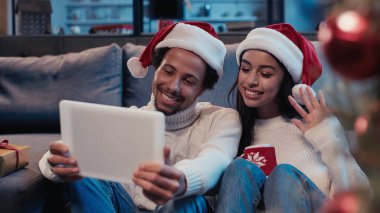 Mutlu Afro-Amerikan erkeği, video araması sırasında kadının yanında el sallıyor ve dijital tablete bakıyor.