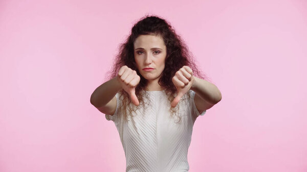 displeased young woman showing thumbs down isolated on pink