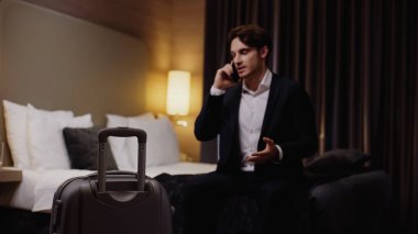 Bulanık genç işadamı otel odasındaki bavulun yanında akıllı telefondan konuşuyor.