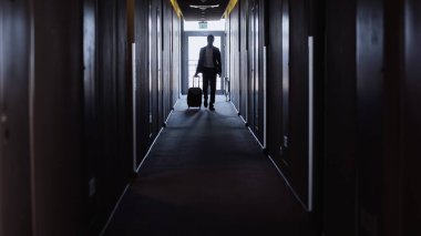 Bavullu bir işadamı otel koridorunda yürüyor.