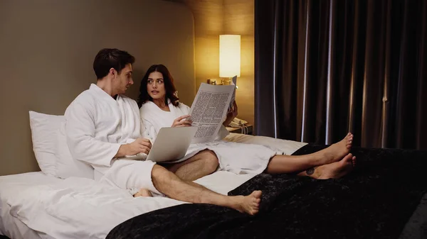 Man Using Laptop Talking Girlfriend Holding Newspaper Hotel Room — Stock Photo, Image