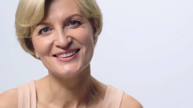 Mutlu, orta yaşlı, temiz yüzlü, kameraya gülümseyen beyaz tenli kadın.