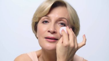 Beyaz üzerine izole edilmiş kozmetik şişirme ile yüz temeli uygulayan orta yaşlı kadın