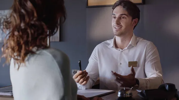 smiling hotel receptionist talking with blurred woman at hotel counter