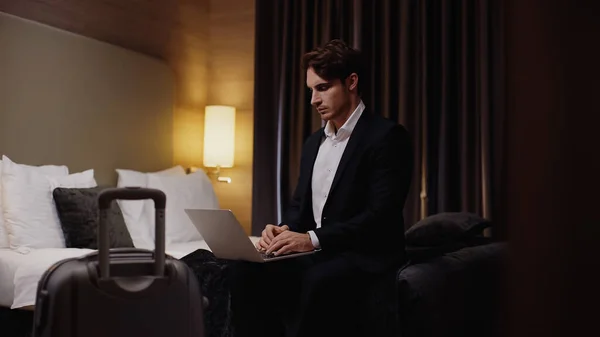 Young Serious Businessman Sitting Bed Using Laptop Luggage Hotel Room — Stock Photo, Image