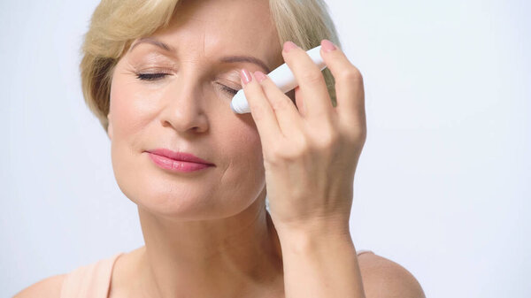 blonde middle aged woman using eye roller isolated on white