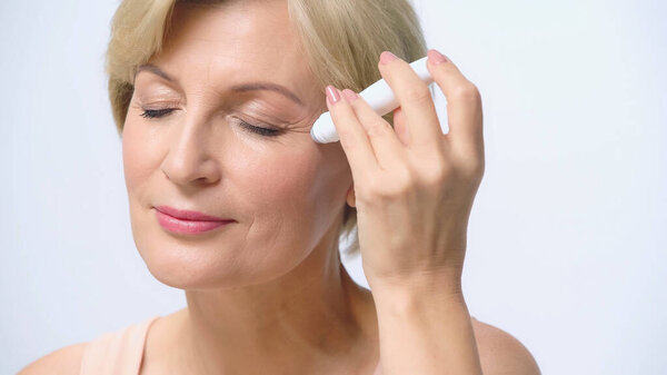 blonde middle aged woman using gel roller on face isolated on white