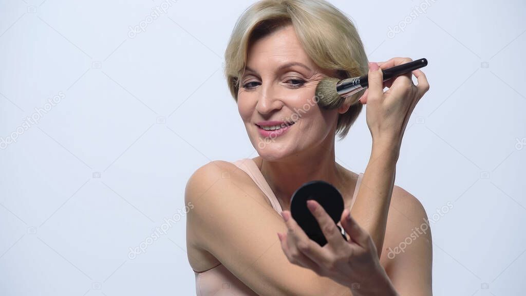 smiling middle aged woman applying face powder isolated on white