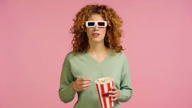 Üç boyutlu gözlüklü endişeli bir kadın elinde patlamış mısır kovası tutarken pembe renkli bir film izliyor.