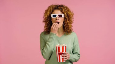 Üç boyutlu gözlüklü gergin bir kadın pembe bir kovayla film izliyor.