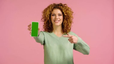 Pembe ekranda izole edilmiş yeşil ekranlı cep telefonunu gösteren bulanık, neşeli bir kadın.