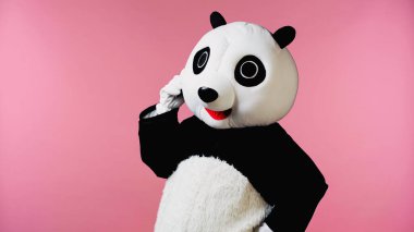 Panda kostümlü düşünceli bir insan elini kalçasına koyup pembe üzerinde duruyor. 