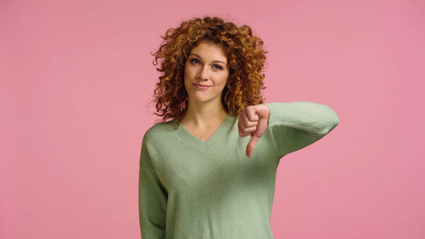displeased redhead woman looking at camera and showing dislike isolated on pink