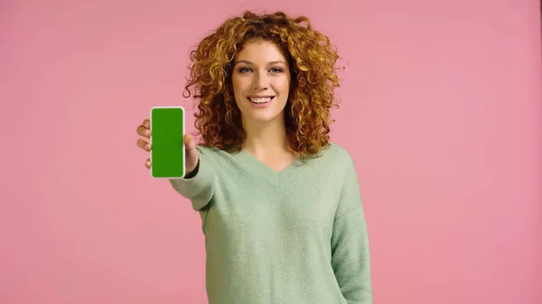 一个快乐的红头发女人看着相机 同时展示智能手机上的绿色屏幕与粉色隔离 — 图库照片