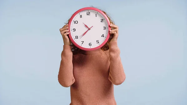 young woman obscuring face with white wall clock isolated on blue