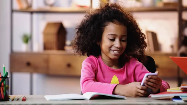 Cheerful African American Child Using Smartphone While Doing Homework — Stock Photo, Image