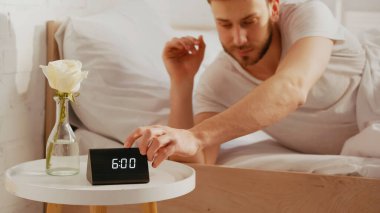 Blurred man turning off clock near flower on bedside table  clipart