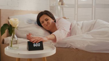 Disappointed woman turning off clock in bedroom in morning  clipart