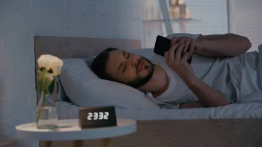 Genç adam gece yatakta akıllı telefon kullanıyor. 