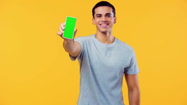 Tişörtlü neşeli genç adam sarı ekranda yeşil ekranlı akıllı telefonu gösteriyor. 