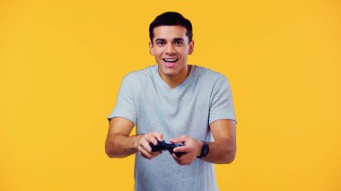 KYIV, UKRAINE - 22 ARALIK 2021: heyecanlı genç adam joystick tutuyor ve sarı üzerinde izole video oyunu oynuyor