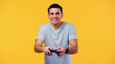 KYIV, UKRAINE - 22 ARALIK 2021: joystick tutan ve sarıda izole video oyunu oynayan neşeli genç adam