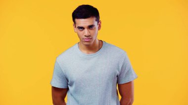Tişörtlü yakışıklı bir adam sarıya izole edilmiş kameraya bakıyor.