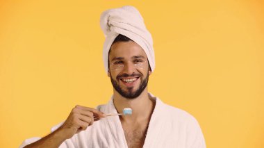 Sarı üzerinde diş fırçası tutan, göz bantlı gülümseyen adam.